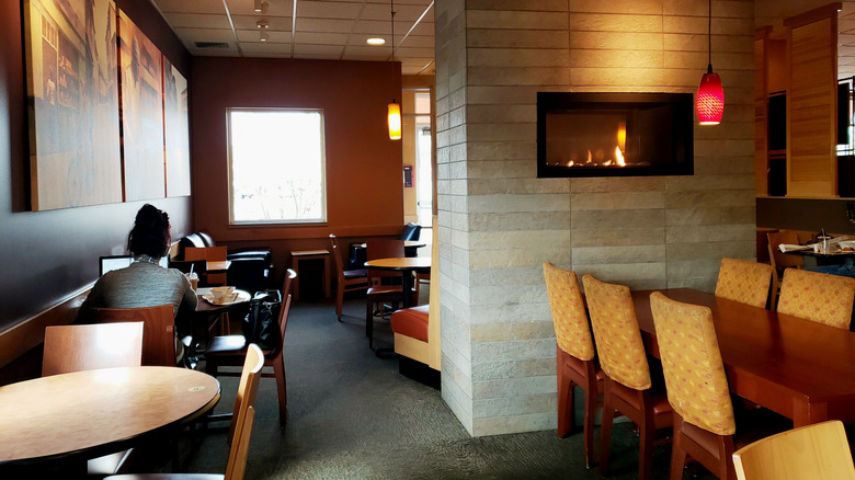 An empty Panera cafe except for one woman on a laptop on left side, fireplace burning on right side