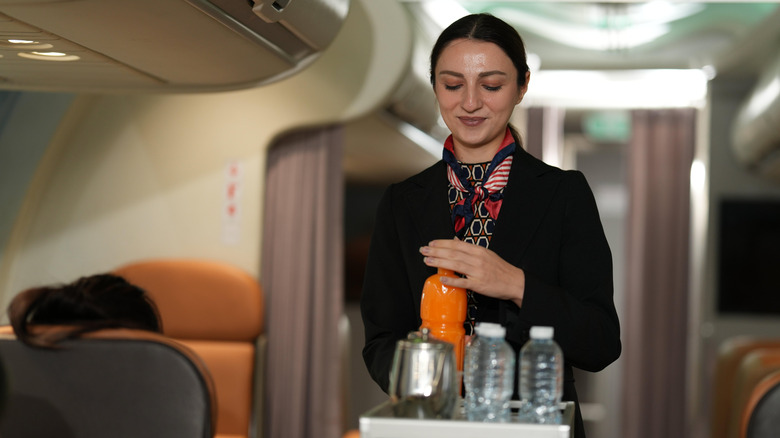 A flight attendant pushing a drink cart down a plane aisle.