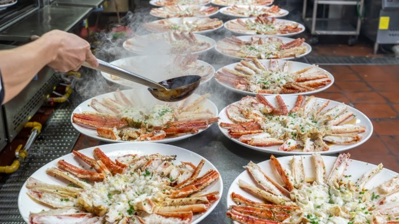 A chef putting the finishing touches on plates of Alaskan king crab legs lined up on a commercial kitchen counter.