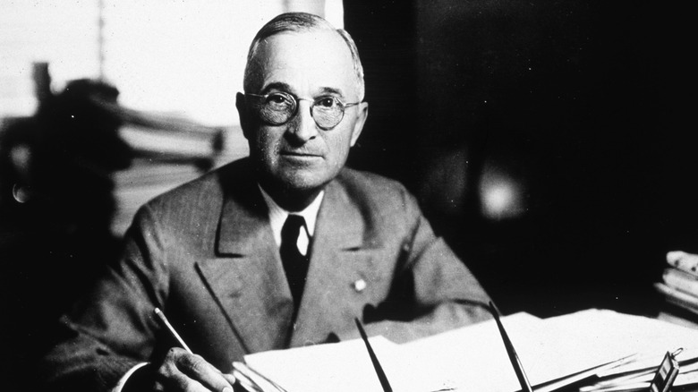 A black and white photo of President Harry S. Truman behind a desk