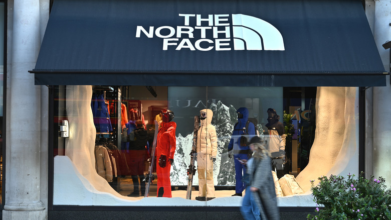 woman wearing cap walks past window display of The North Face