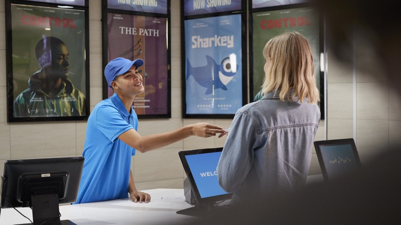Woman paying for movie at the cinema with movie posters in the background