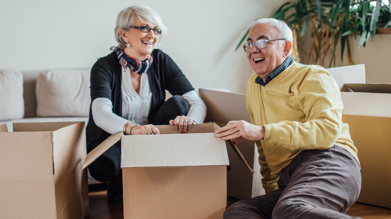 Mature couple smiling and packing cardboard boxes in a living room.