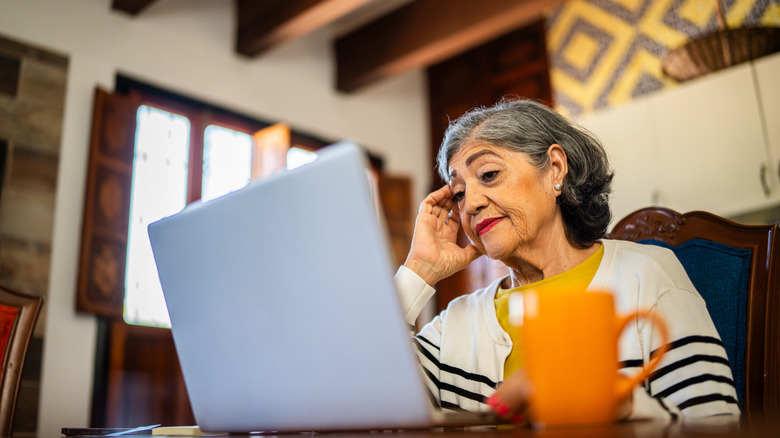 A mature woman looking at her laptop with a worried expression.