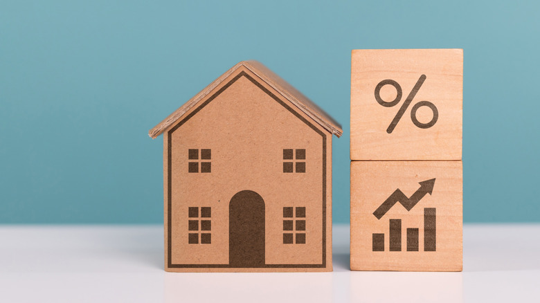 Small wooden home next to wooden percentage block on top of wooden block arrow and chart bars