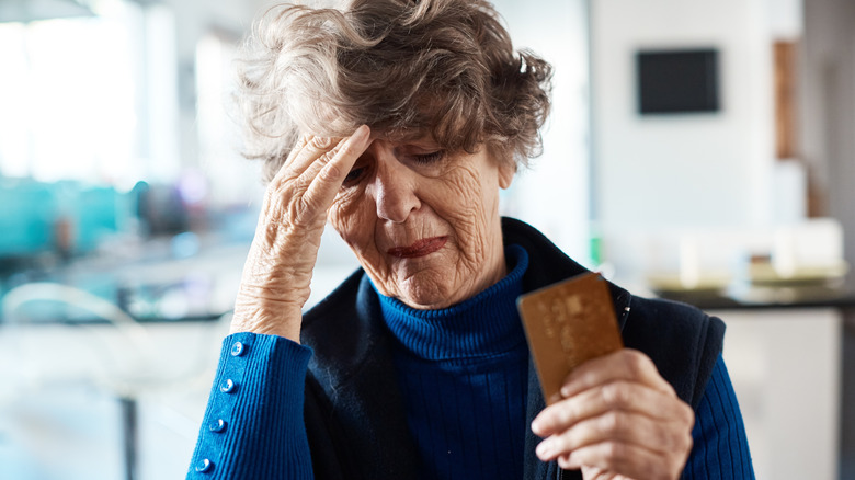 Older mature woman toucles forhead while holding credit card