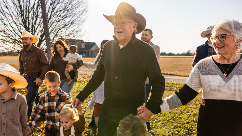 An smiling elderly man wearing a cowboy hat outside with grandchildren and family.