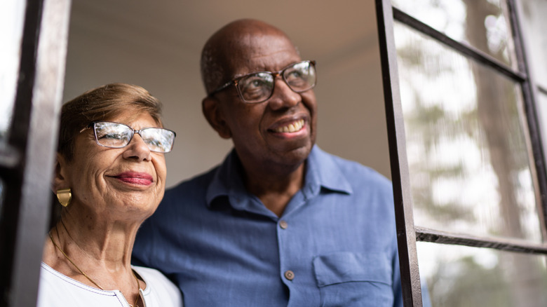A content senior couple looking through the window at home.