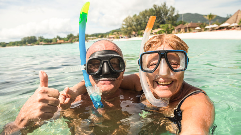 A smiling senior couple wearing snorkels in the ocean from a selfie point of view.