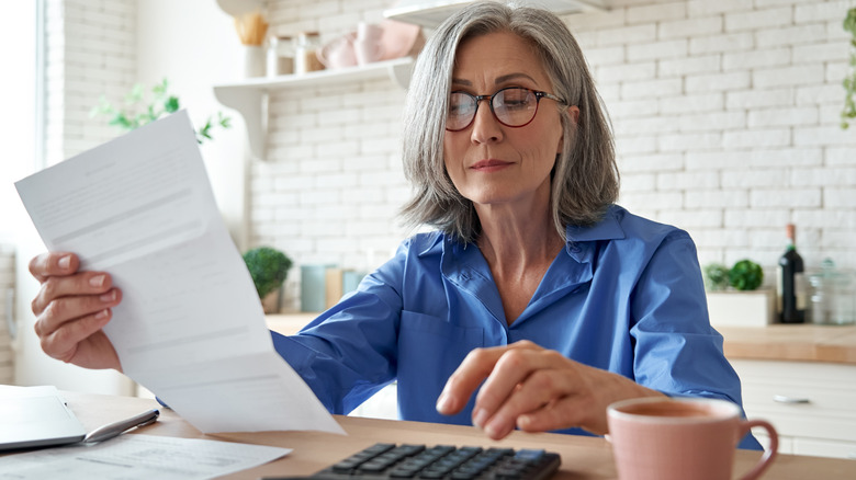 Gray-haired lady in kitchen who is figuring out a bill.