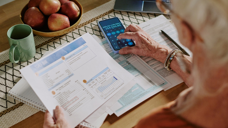 Old woman figures out expenses with calculator smart phone app.
