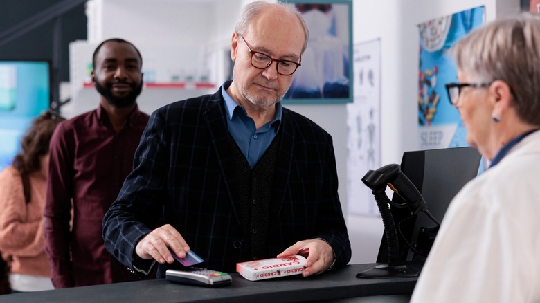 Older man paying by card for medication at a pharmacy counter