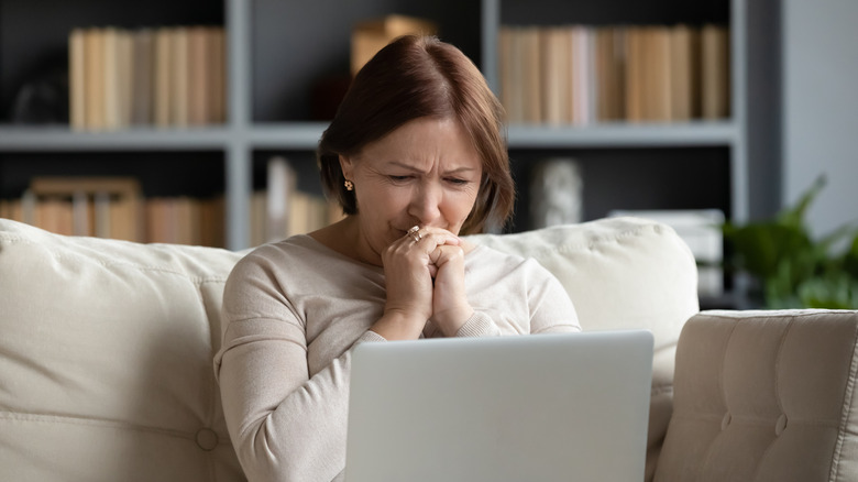 An older woman looking upset while staring at her laptop