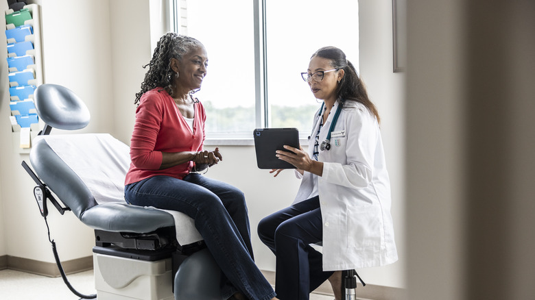 Female doctor and senior woman looking at digital tablet in exam room.