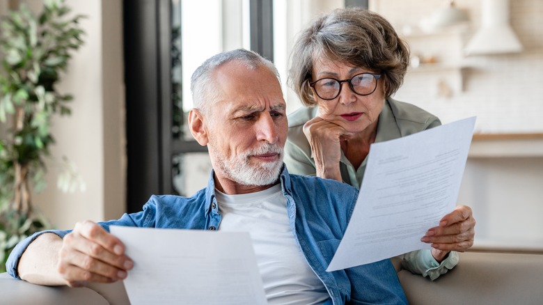 Senior old elderly spouses grandparents reading documents, having issue problem debt with money loss, doing paperwork together at home.