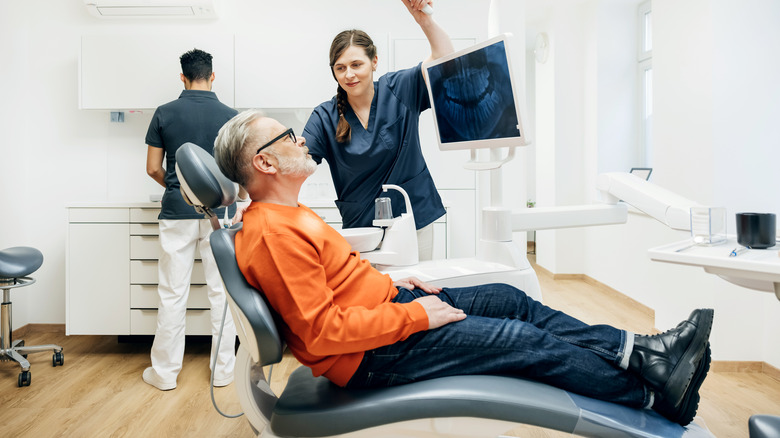 A dental assistant adjusting an overhead light during a check up on a patient sitting back in a mechanical chair while the orthodontist prepares for a procedure.