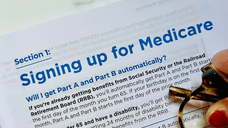 A hand holding glasses rests on the sign-up page of the 2025 Medicare booklet