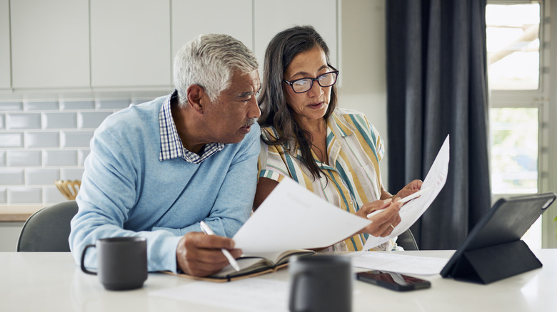 An older couple is sitting at their kitchen table reviewing financial documents.