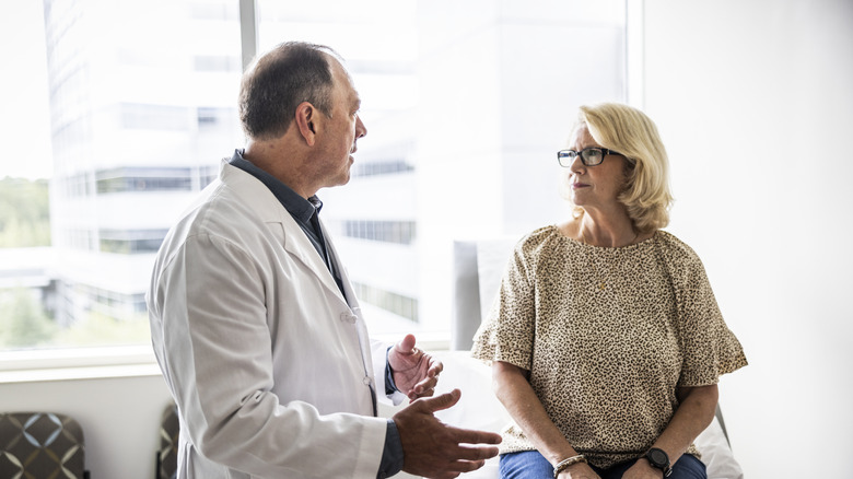Senior male doctor consulting with senior woman in exam room.