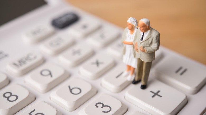 retired couple figurines standing on calculator