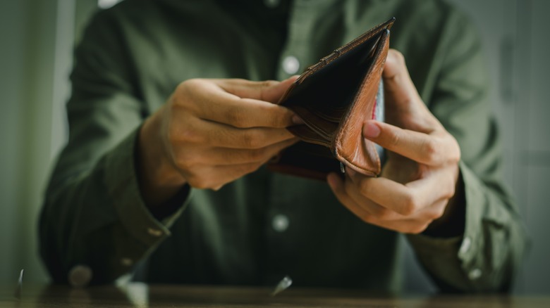 unidentified person in a green shirt holding open an empty wallet