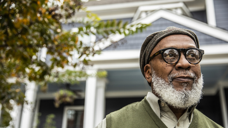 Old man with glasses standing in front of a house