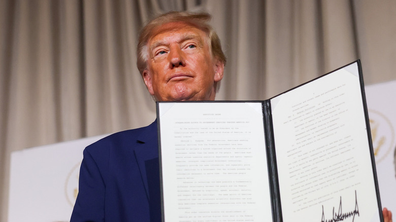 President Donald Trump holding up a signed executive order in the Oval Office during his second term.