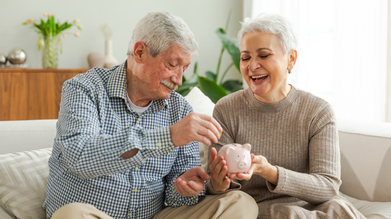 retired couple putting money in piggy bank