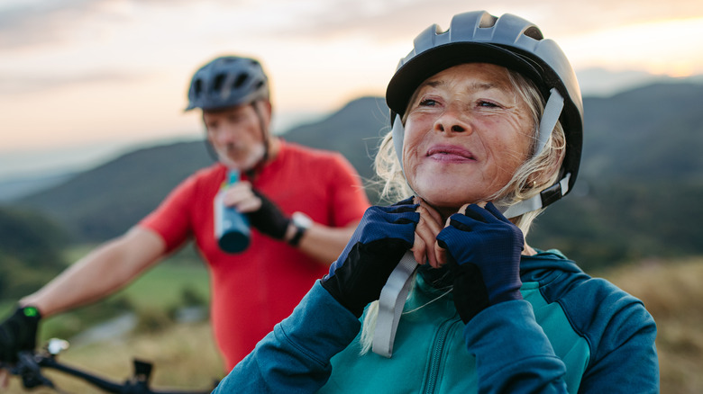 older woman adjusts bike helmet as man sips drink in background