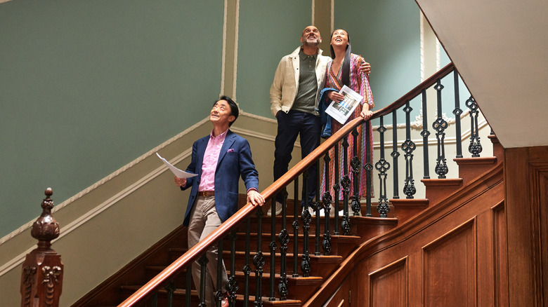 Real estate agent walking down staircase in large house with wealthy couple