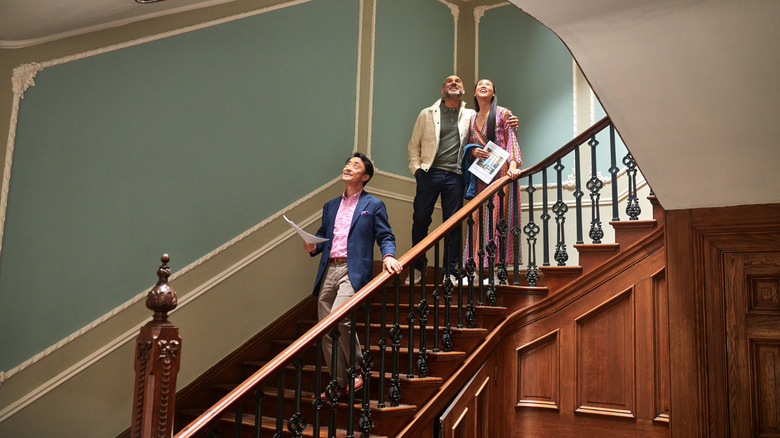 Real estate agent walking down staircase in large house explaining to wealthy couple the features of potential new home