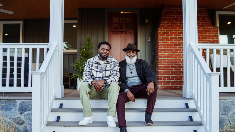 A senior man and his Millennial son sitting on the front porch steps of a home.