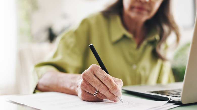 Close up of woman's hand writing with pen as she sits in front of a laptop