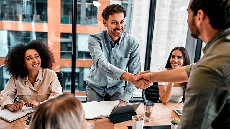 A Millennial man being congratulated on a promotion during an office meeting.