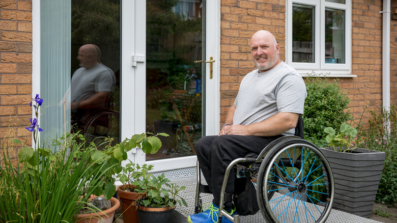 A man in a wheelchair outside his home on an accessibility ramp.