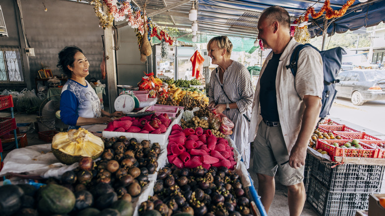 Older tourist couple speaking with local woman at market