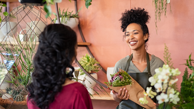 Young store owner holding flowers talking with a customer