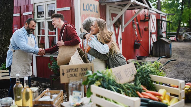 Young couple embracing older couple selling local farm goods