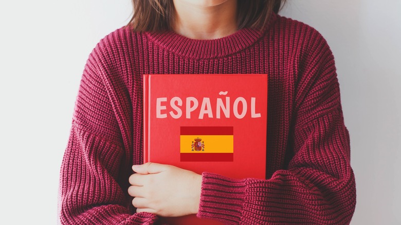 Woman in red sweater holds Spanish dictionary in her folded arms