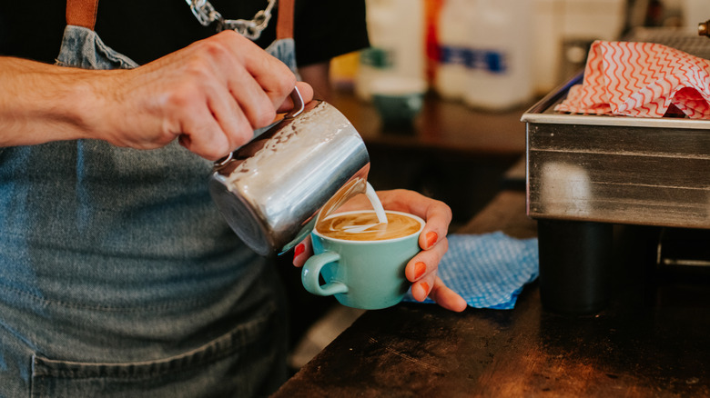 A close-up of a barista making a delicious latte coffee with milk.