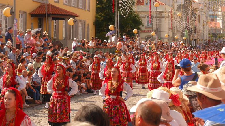 Women dressed in traditional Portugeuse clothing in a parade with people watching from the sidelines.