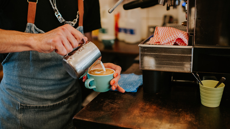 A close-up of a barista making a delicious latte coffee with milk.