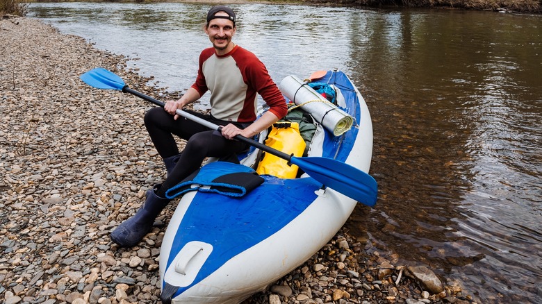 Smiling man with inflatable kayak and paddle by water