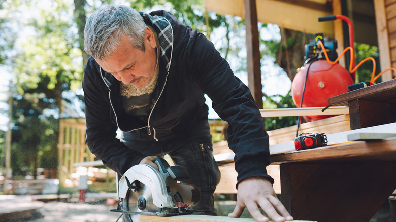 Carpenter cutting wooden board for log cabin with handle circular saw grinder