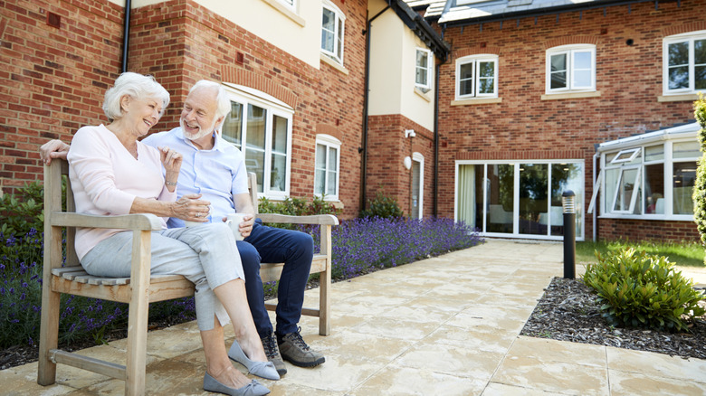 Older couple sitting on a bench outside of a retirement community