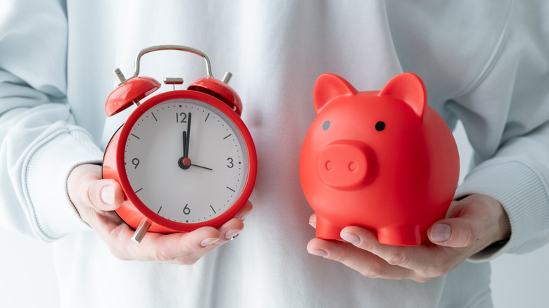 A person holds a piggy bank and clock in their hands