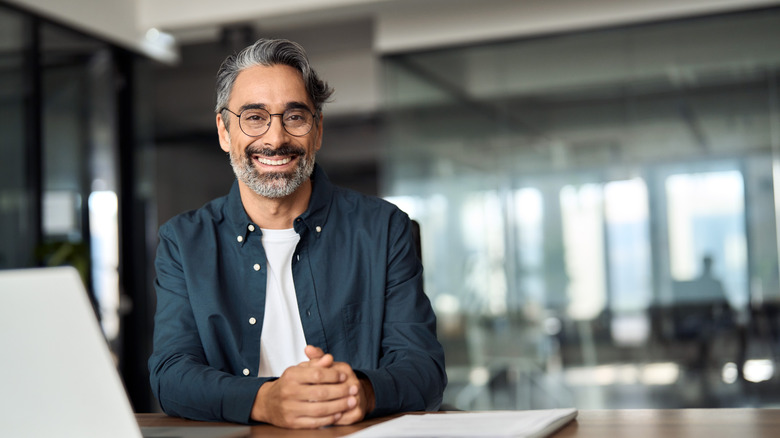 A smiling mature man wearing glasses and shirt sitting at office desk