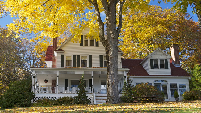 A beautiful colonial-style home in Winsted, CT with wraparound porch and a tree with golden leaves.