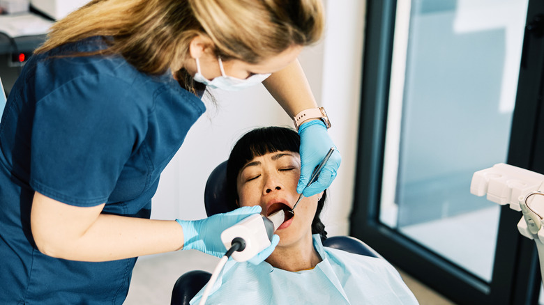 white female dentist exams teeth of Asian female patient