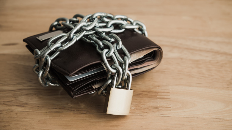 Leather wallet tied up steel chain and padlock on wooden table background.